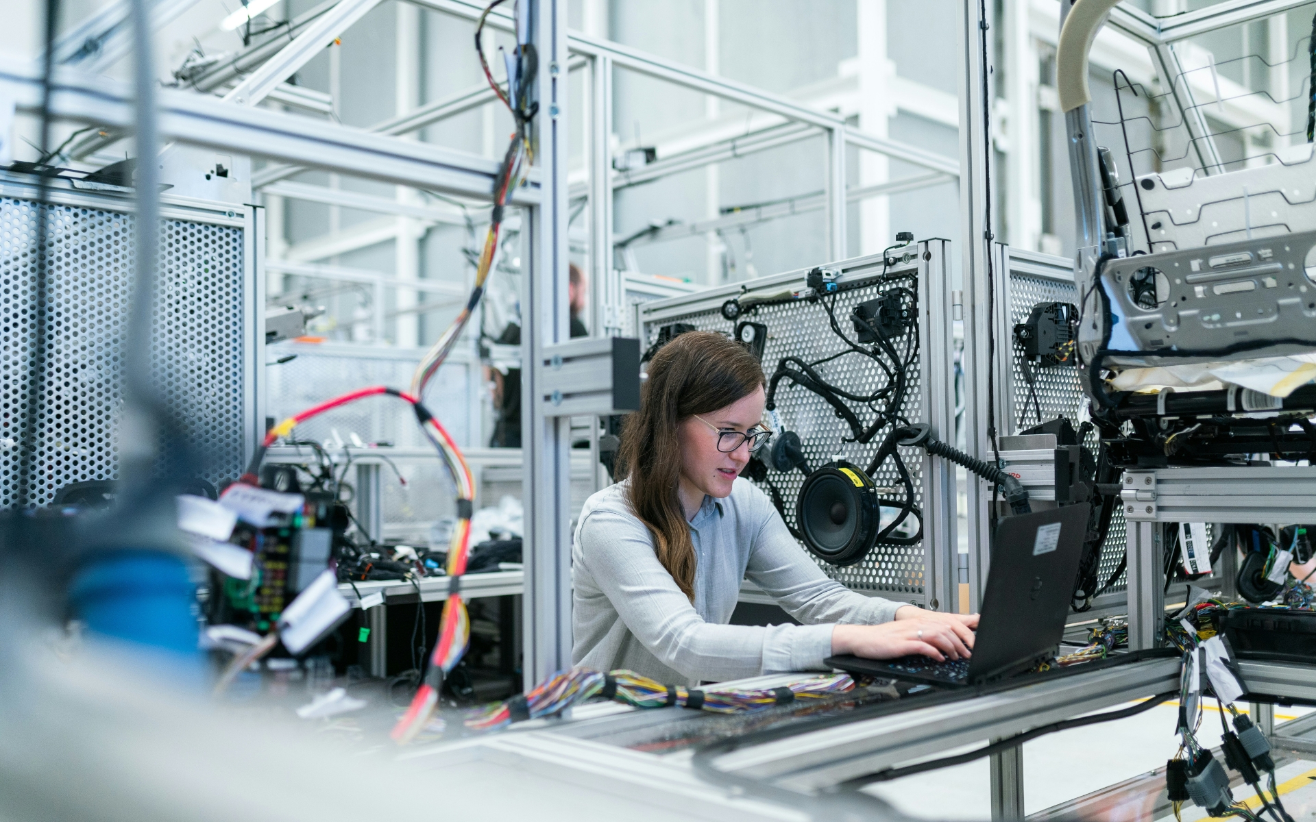 Ingegnera al lavoro con computer portatile lungo una linea di produzione industriale e collaudo componenti