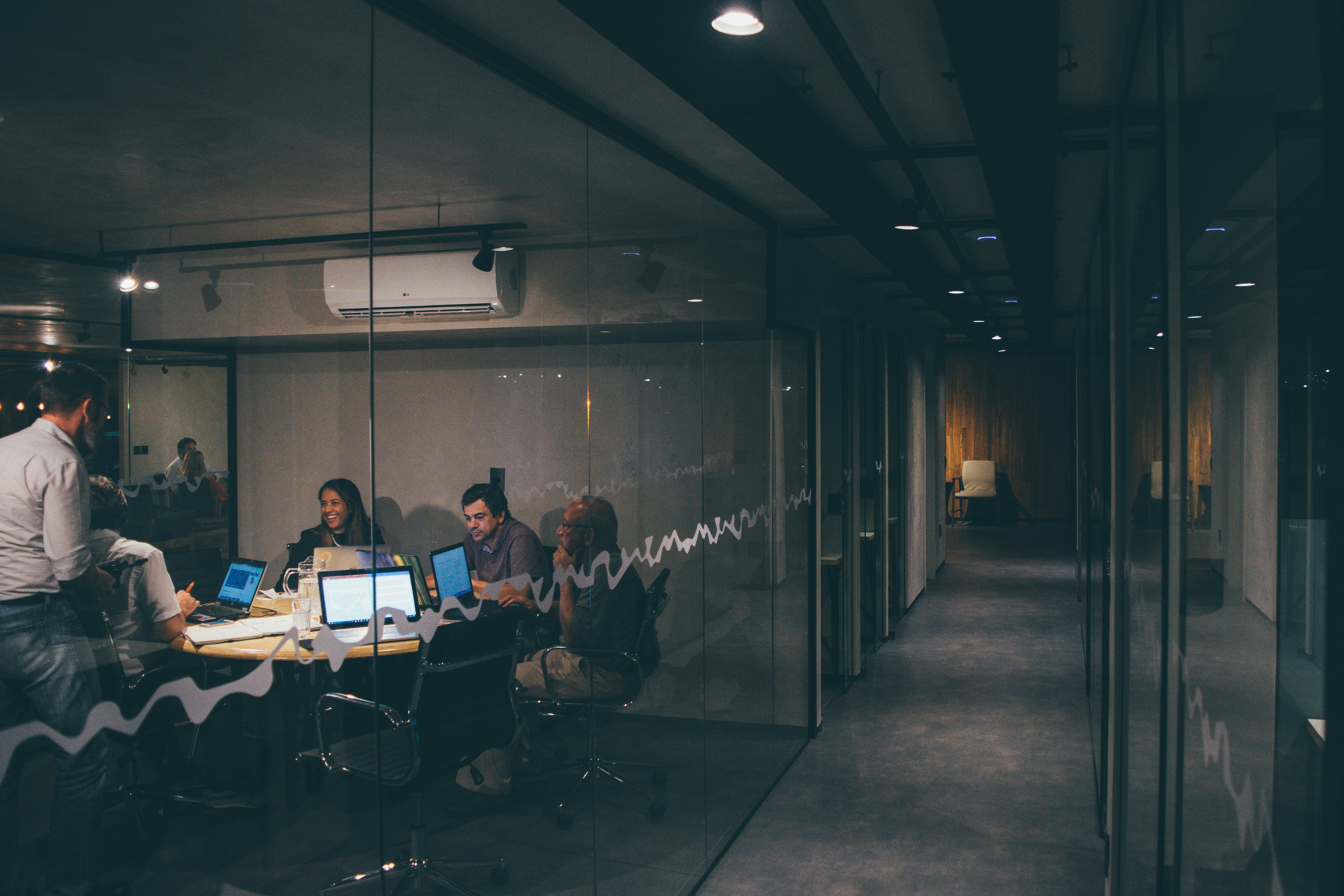 Group of 5 professionals in a meeting in a modern office with glass walls. Laptops and documents on the table.